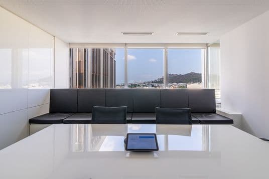 Modern conference room with black couches, a white table, and a tablet. Floor-to-ceiling windows offer a city and mountain view outside.
