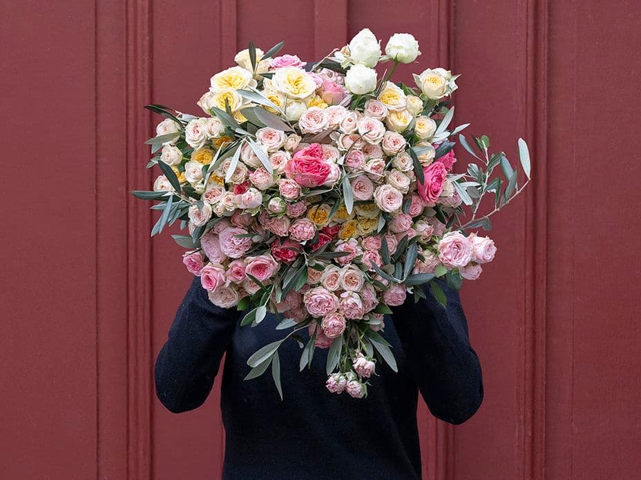Huge bouquet of flowers completely covers the person holding it up in front of a brown and red door