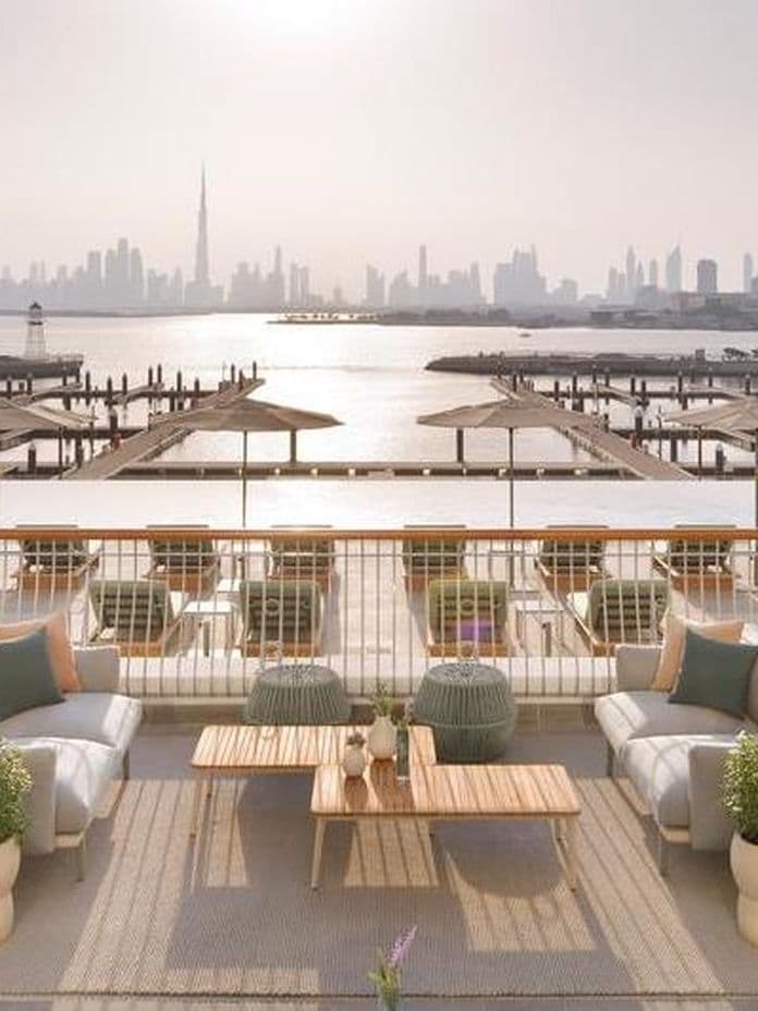 Luxurious rooftop terrace with elegant seating and potted plants, overlooking a city skyline and water at sunset.