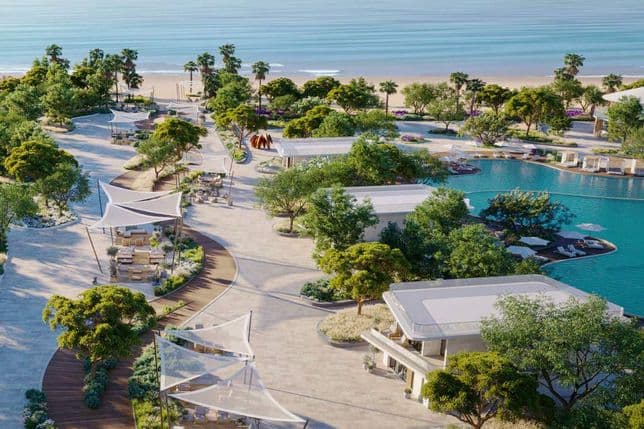 Aerial view of a beachfront resort with modern villas, lush greenery, a swimming pool, and pathways, beside a sandy beach and calm sea.