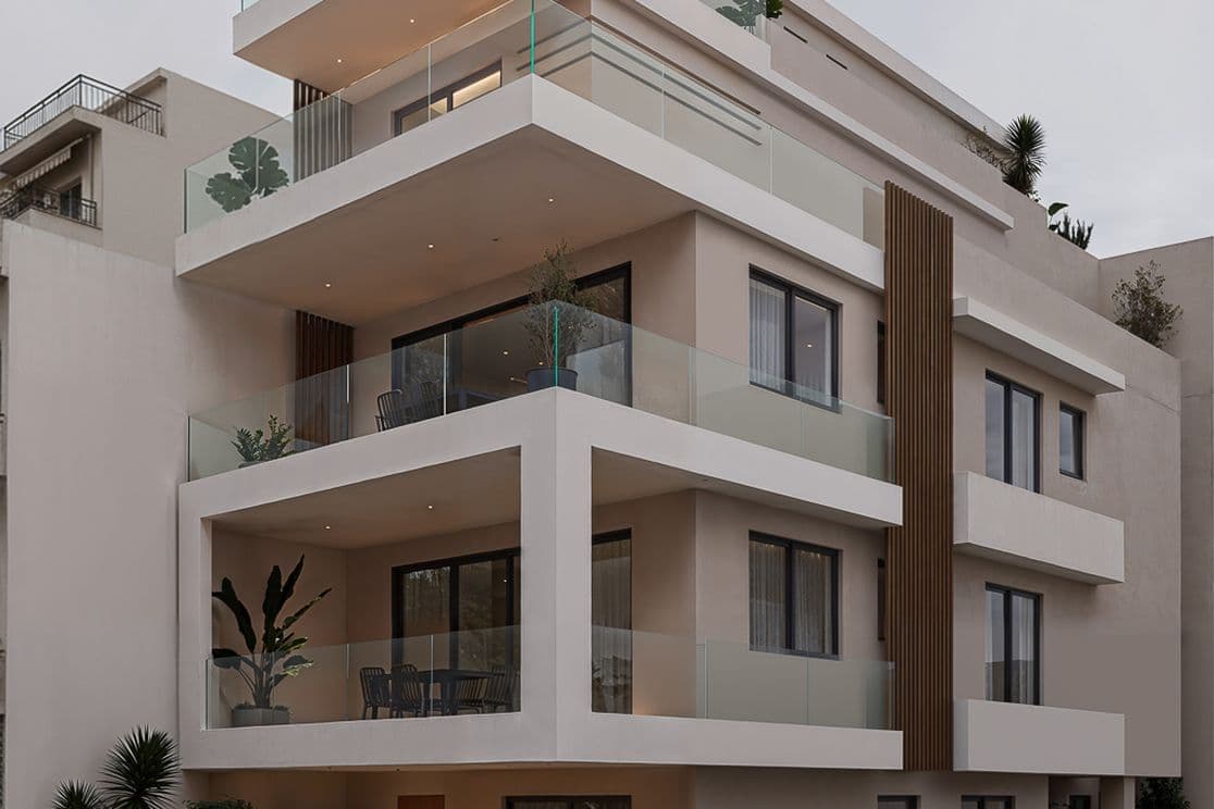 Modern multi-story building with glass balconies, large windows, and minimalistic design features on a corner lot. Overcast sky background.