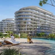 Luxurious beachfront resort with modern, curved buildings, a pool, palm trees, and loungers. People relax under umbrellas. Futuristic buildings nearby.