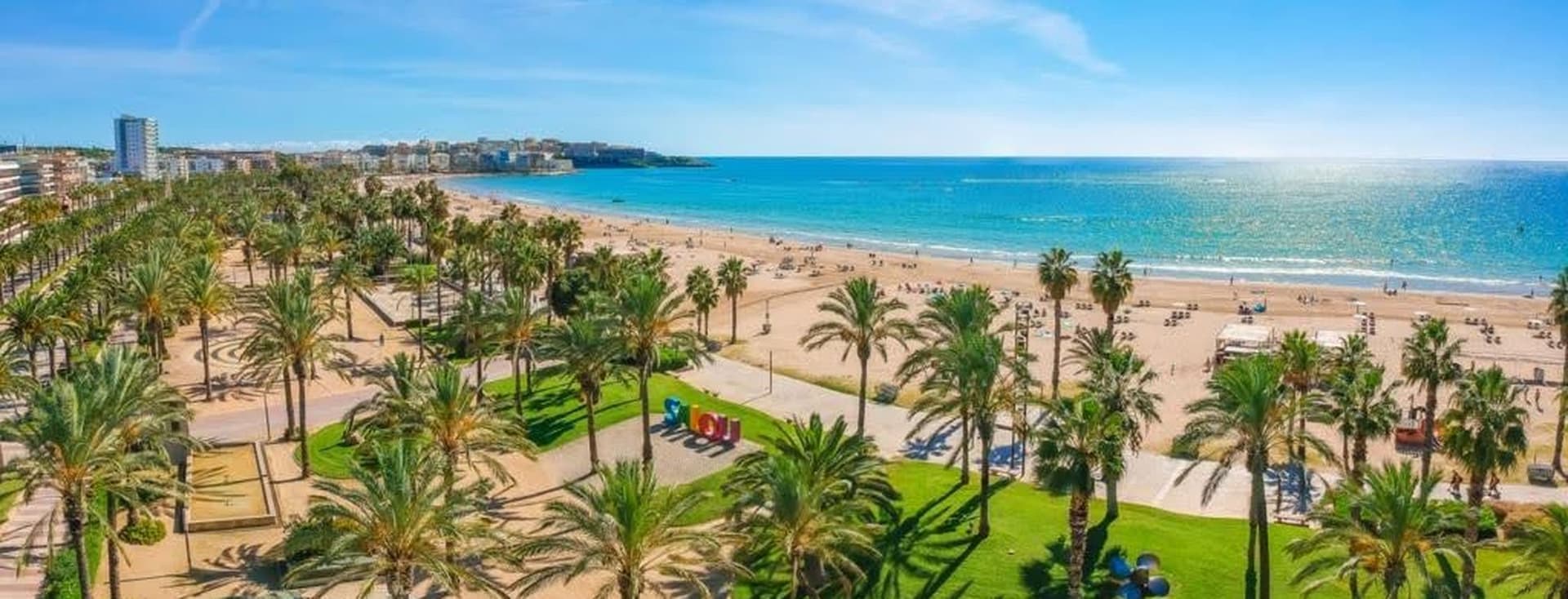 Playa de la Costa Dorada con palmeras, zonas verdes y edificios al fondo