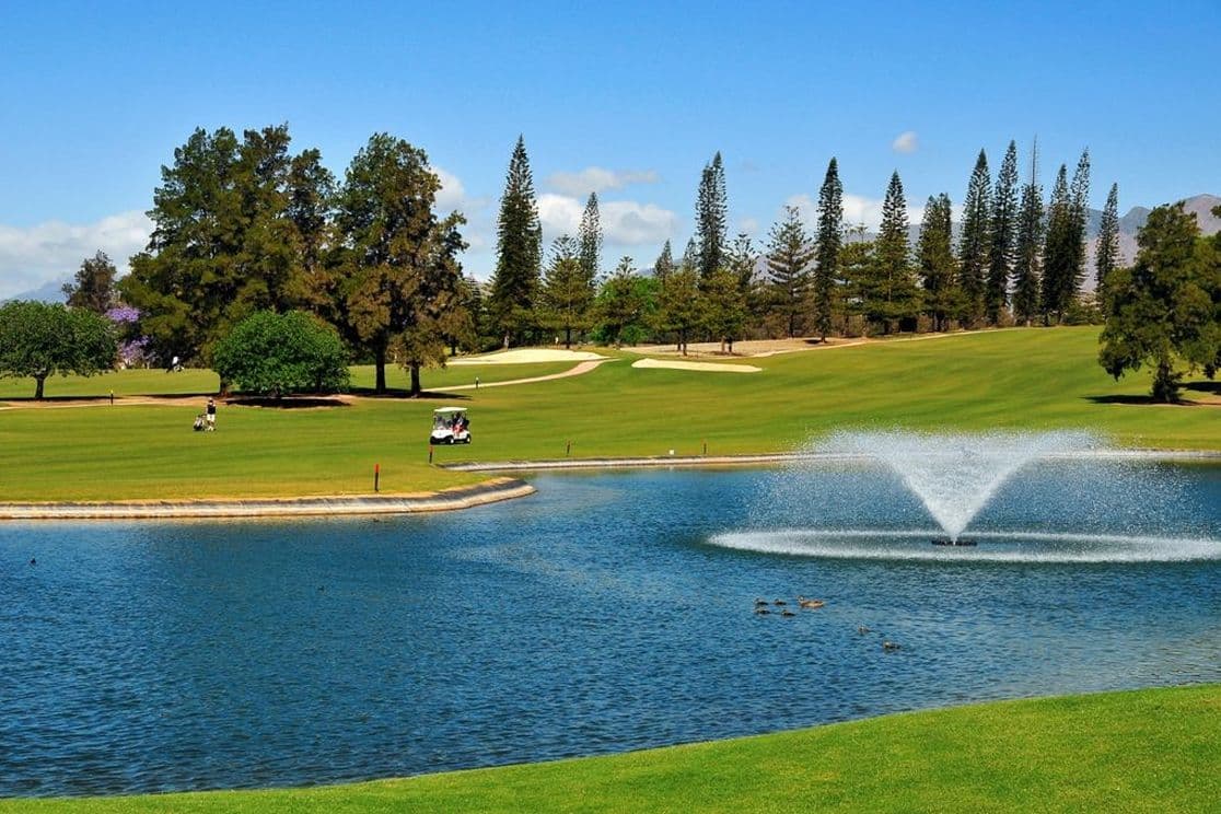 Golfplatz in Mijas mit Spielern, einem Golfwagen und einem See mit einem Brunnen.