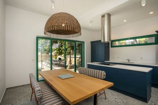 Modern kitchen and dining area with wooden table, woven pendant light, blue cabinetry, and large sliding doors opening to an outdoor patio.