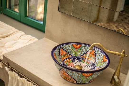 Decorative ceramic sink with colorful patterns and brass faucet set on a concrete countertop in a stylish bathroom.