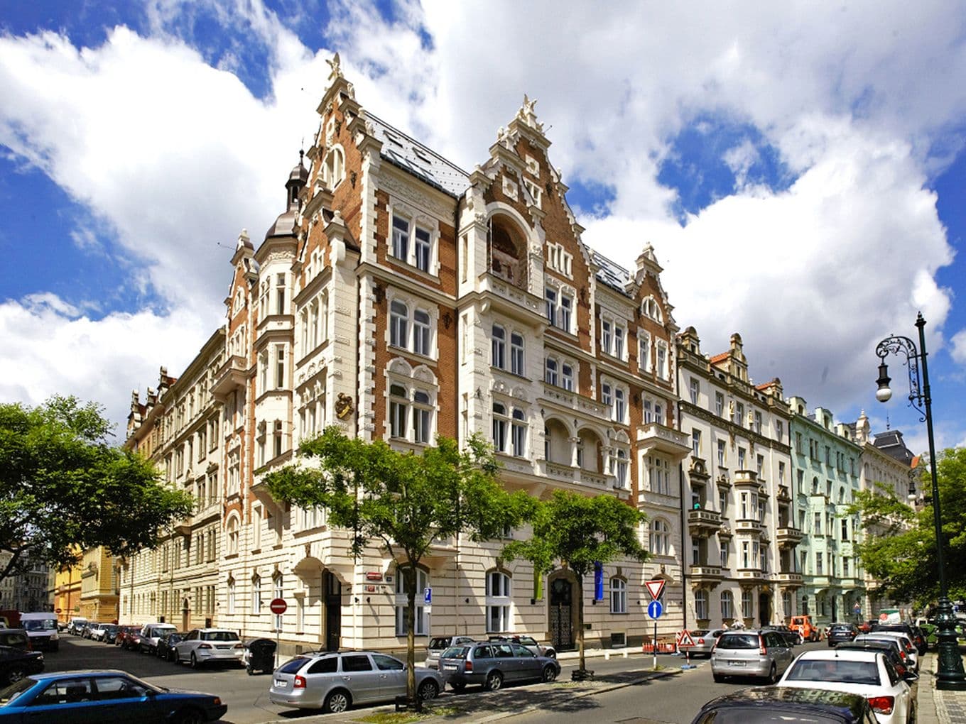 Detailed view of a historic apartment building with a red brick facade, white stucco elements, and an ornate turret. A typical example of Art Nouveau architecture in Prague, with a mansard roof and rich decoration.