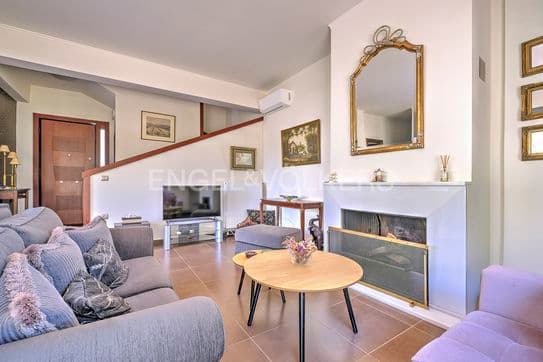 Living room with gray sofa, round wood table, and white fireplace with gold mirror. Brown tile floor.