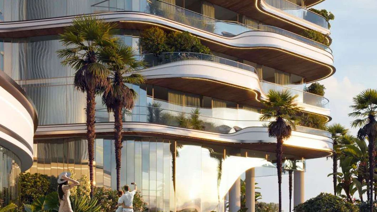 Modern building with wave-like balconies, lush greenery, and palm trees. People are walking beside a reflective pool under a clear sky.