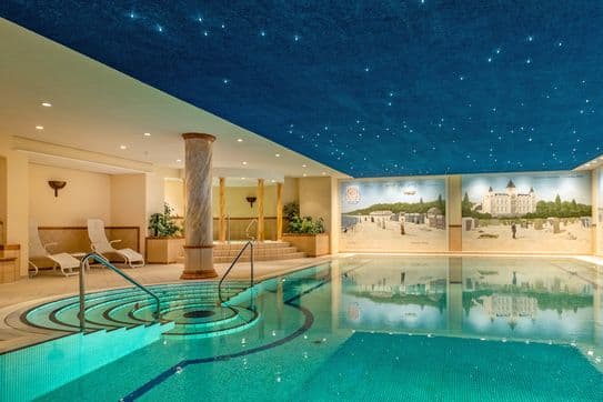 Ein Innenpool mit Mosaikfliesen, runden Stufen und Handläufen, einer sternenblauen Decke, Liegestühlen und großen, malerischen Wandgemälden entlang der Wand