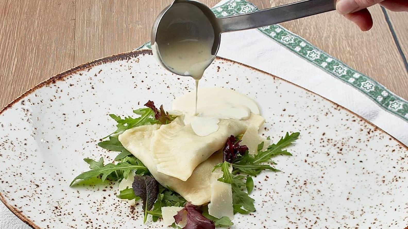 Tiroler Teigtaschen mit frischem Salat und Sahnesauce, angerichtet auf rustikalem Porzellanteller.
