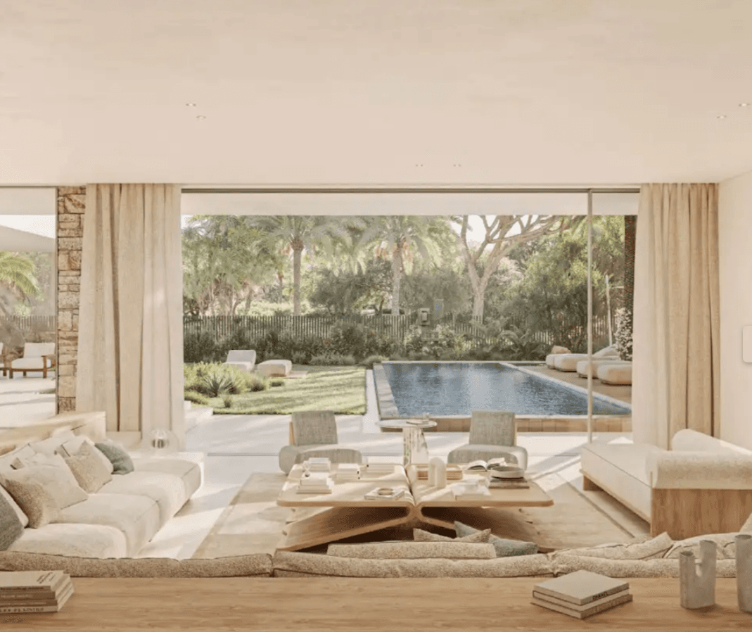 Modern living room with neutral tones, large windows, and a view of a pool surrounded by lush greenery and palm trees.