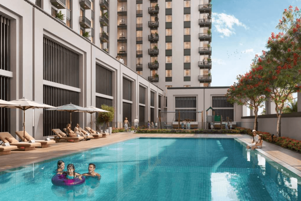 Outdoor swimming pool at Odessa with sun loungers, landscaped areas, and the residential tower in the background, showing families enjoying the water.