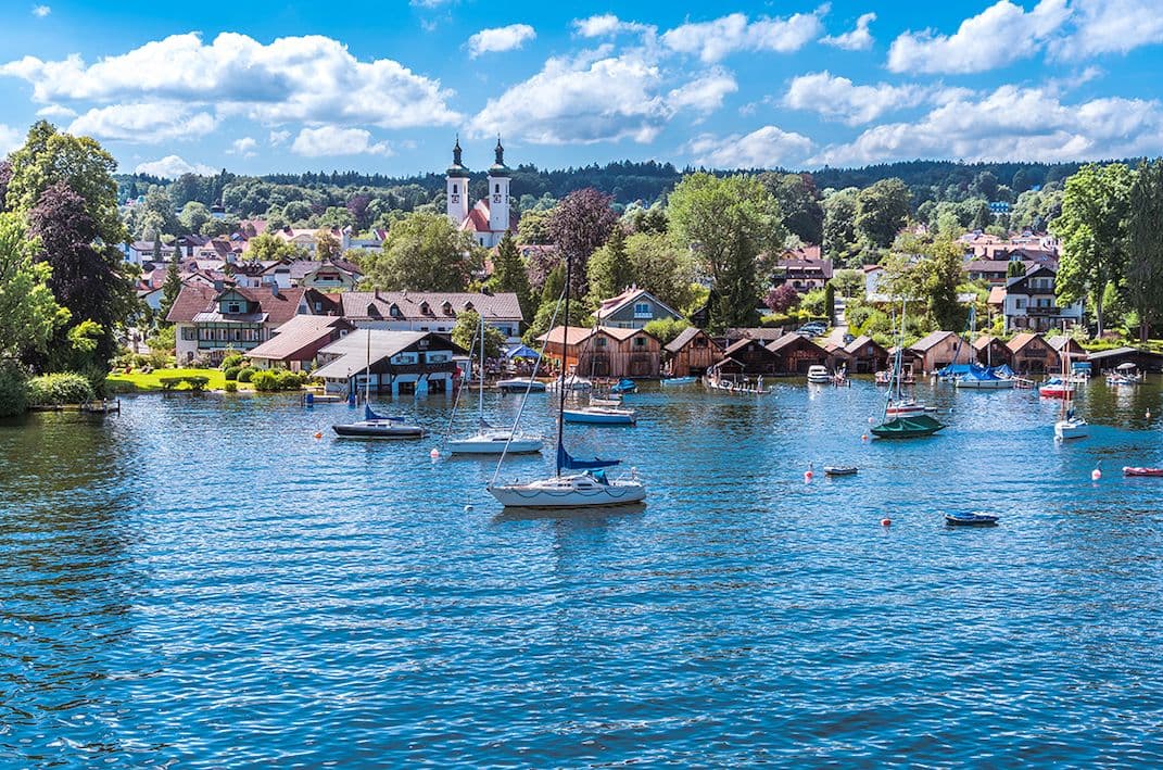 Summer view of Tutzing on Lake Starnberg with sailboats, St. Joseph church, lakeside homes and lush Bavarian landscape