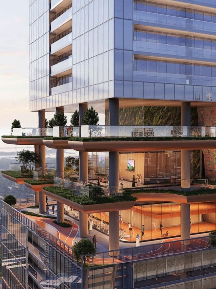 Modern high-rise building with multiple open-air terraces, greenery, and glass walls overlooking a cityscape and distant water view.