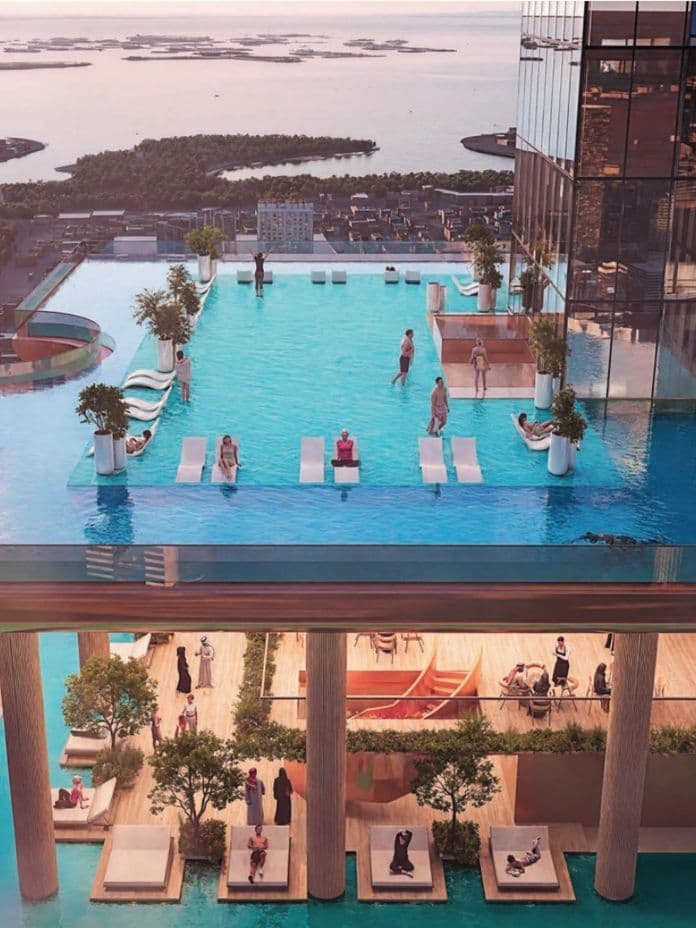 Rooftop infinity pool with people lounging and swimming, overlooking a coastal cityscape at sunset. Luxurious seating areas below the pool.