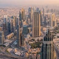 Aerial view of a cityscape with modern skyscrapers, intricate road networks, and surrounding urban buildings under a hazy sky.