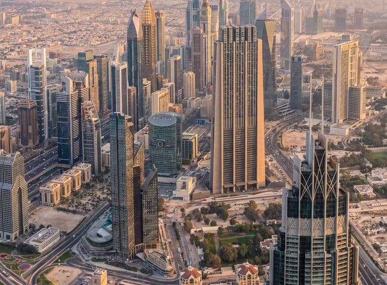 Aerial view of a cityscape with modern skyscrapers, intricate road networks, and surrounding urban buildings under a hazy sky.