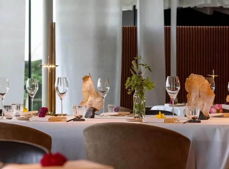 Elegant dining table set with wine glasses, plates, and a glass vase of greenery; rock-like centerpieces and a modern interior with white columns.