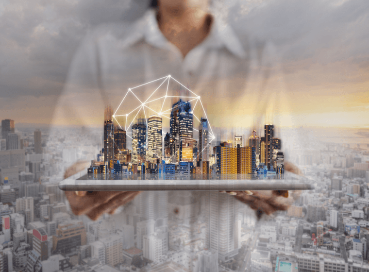 Eine Person hält ein Tablet, auf dem eine virtuelle Stadtlandschaft mit geometrischen Linien dargestellt ist, die in einen realen Stadthintergrund bei Sonnenuntergang übergeht.
