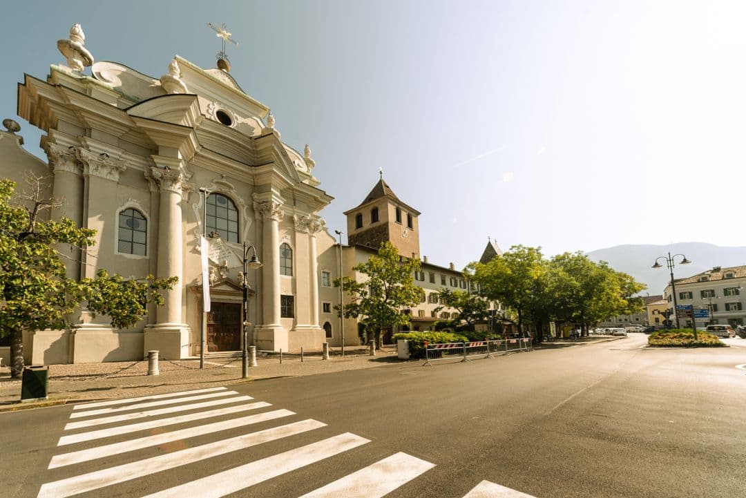 A historic European church with ornate architecture stands beside a cobblestone street and zebra crossing, under a clear blue sky.
