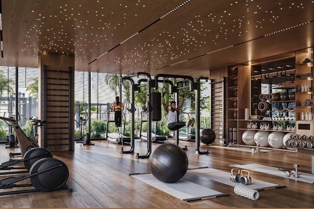 Modern gym with wooden floors and a starry ceiling, bright windows, people using machines, mats, kettlebells, and a large exercise ball.