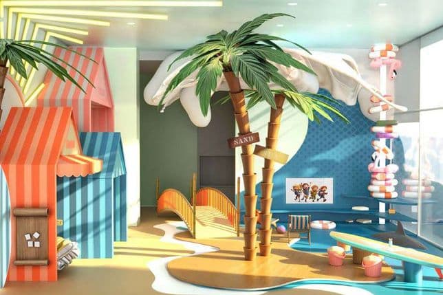 Vibrant beach-themed kids’ playroom with colorful cabanas, palm-tree structures, surfboards, slides, and soft play zones, all set beside large floor-to-ceiling windows bringing in natural light.