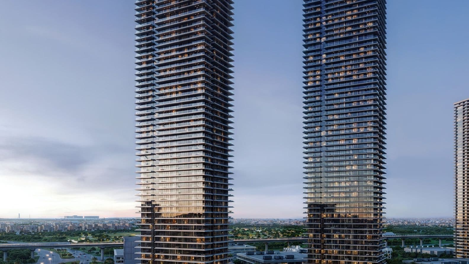 Zwei moderne Wolkenkratzer mit reflektierenden Glasfassaden in der Abenddämmerung, umgeben von Straßen und Grünflächen, unter einem klaren Himmel.