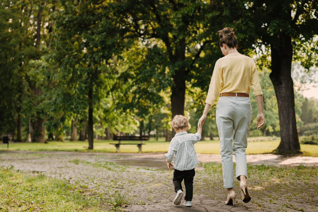 Eine Mutter und ein Kind gehen einen schattigen Weg in einem grueneren Parkbereich von Vindera at The Valley entlang.