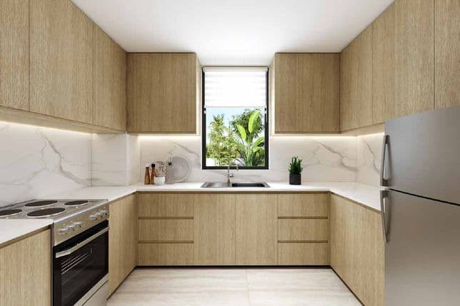 Modern kitchen with light wood cabinets, marble countertops, a stainless steel fridge, and a window view of lush greenery.