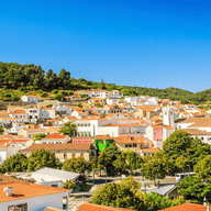 Scenic view of a picturesque town with colorful houses and red-tiled roofs set against a lush, green hillside under a clear blue sky.