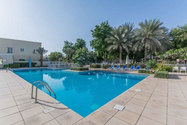 Außenpool mit klarem, blauem Wasser, umgeben von Palmen und Sonnenliegen an einem sonnigen Tag.