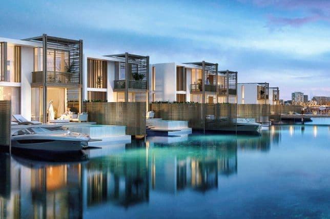 Modern waterfront villas at Mina Rashid illuminated at dusk, each featuring private terraces, pools, and direct yacht docking. The calm water reflects the soft lighting of the villas, creating a serene and luxurious atmosphere.          Ask ChatGPT