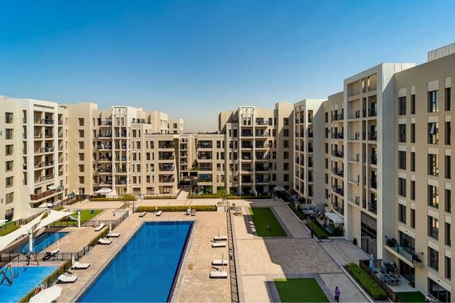 Innenhof eines Apartmentkomplexes in Town Square Dubai mit großem Swimmingpool, Sonnenliegen, schattigem Kinderspielbereich und modernen beigefarbenen Gebäuden.