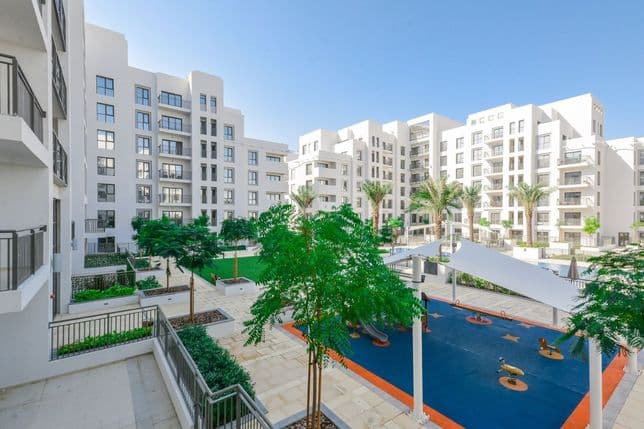 Modern mid-rise apartment buildings in Town Square Dubai with landscaped courtyards and a shaded children's play area featuring colorful rubber flooring.