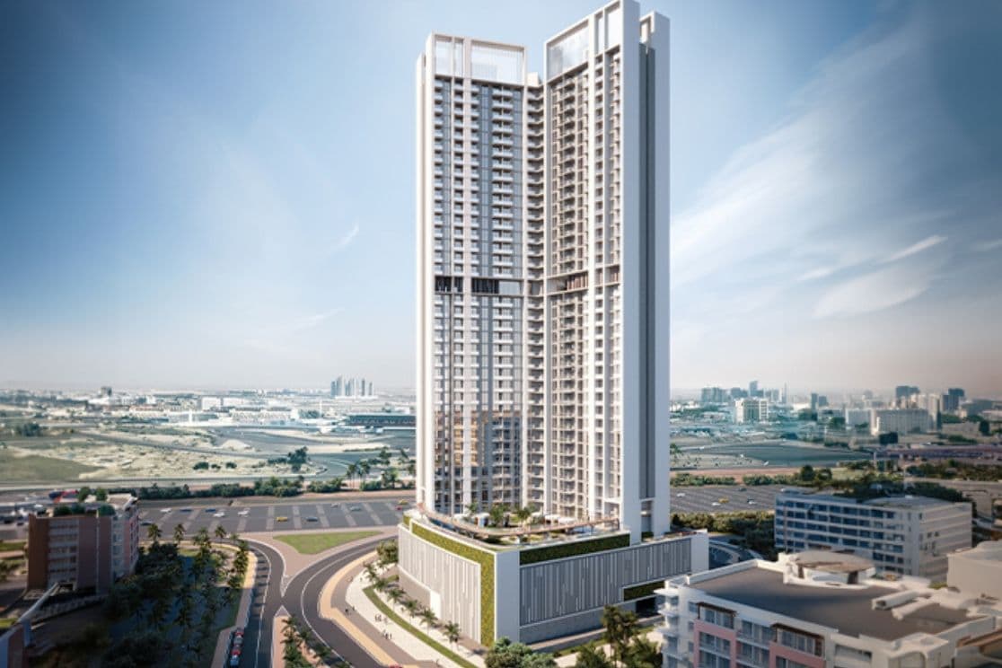 A tall, modern skyscraper with a unique design stands amidst a cityscape under a clear blue sky, surrounded by roads and smaller buildings.