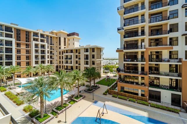 View of apartment buildings surrounding a pool and playground at Town Square Dubai, with palm trees and leisure amenities in a family-friendly setting.