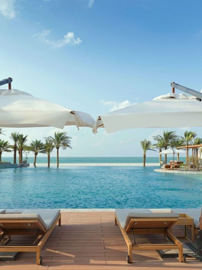 Luxury beach resort pool with sun loungers and umbrellas facing the ocean.