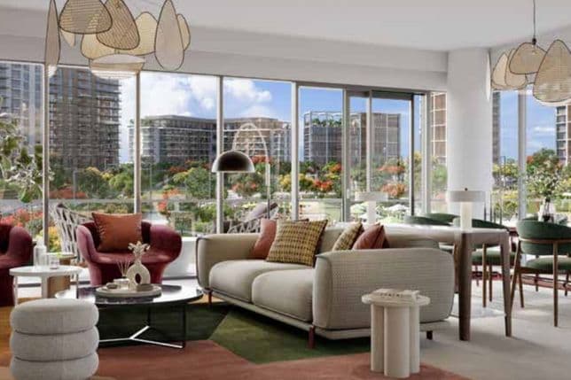 Modern living room with large windows, stylish furniture, and colorful decor. Overlooks a cityscape with greenery and tall buildings.