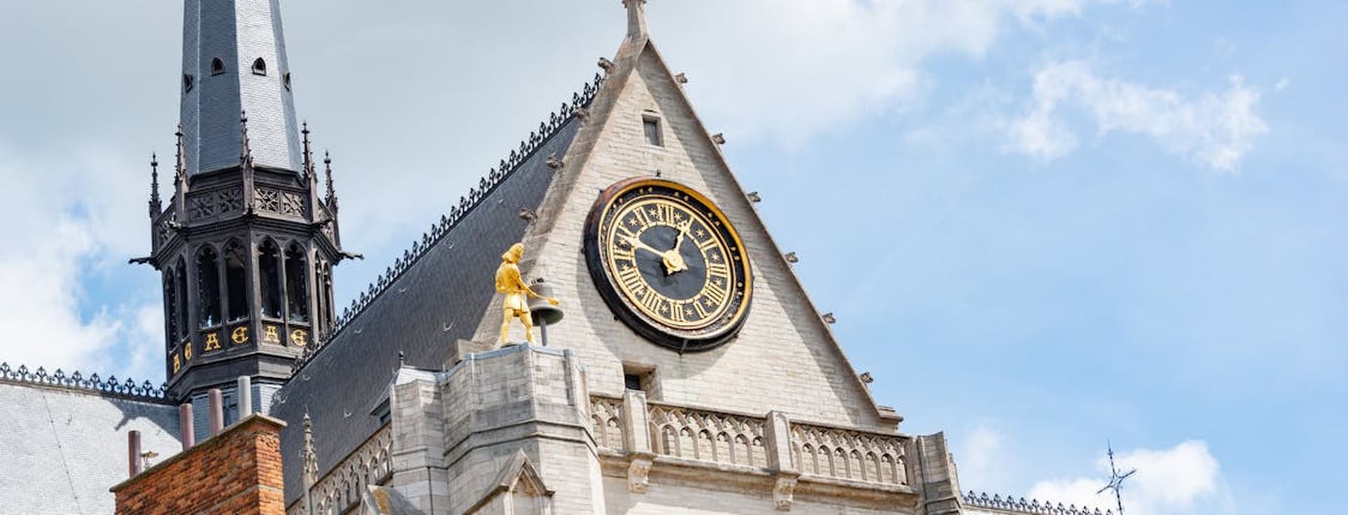 Buitenaanzicht van de Sint-Romboutskathedraal in Mechelen, België, met een klok, torenspits en gouden beeld tegen een blauwe lucht.
