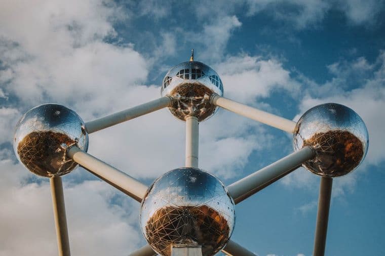 Het Atomium in Brussel, België, is een stalen constructie van negen zilveren bollen die door buizen met elkaar zijn verbonden tegen een blauwe lucht met wolken.