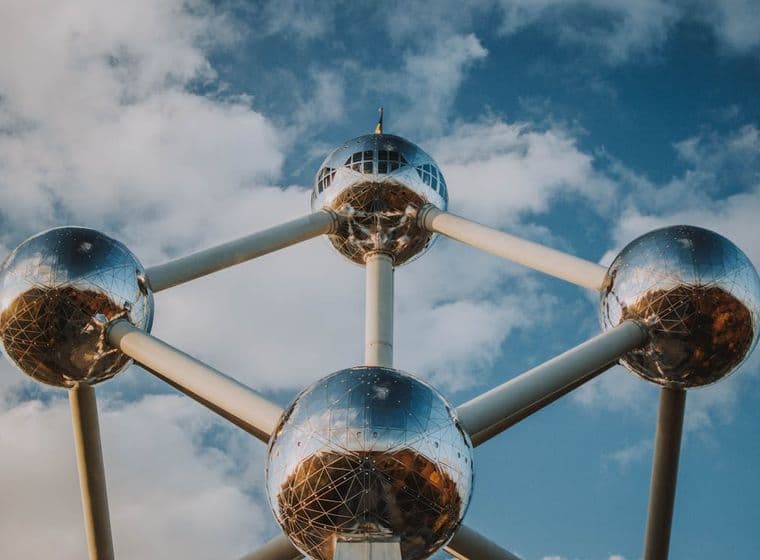 L'Atomium à Bruxelles, en Belgique, est une structure en acier composée de neuf sphères argentées reliées par des tubes, le tout se détachant sur un ciel bleu nuageux.