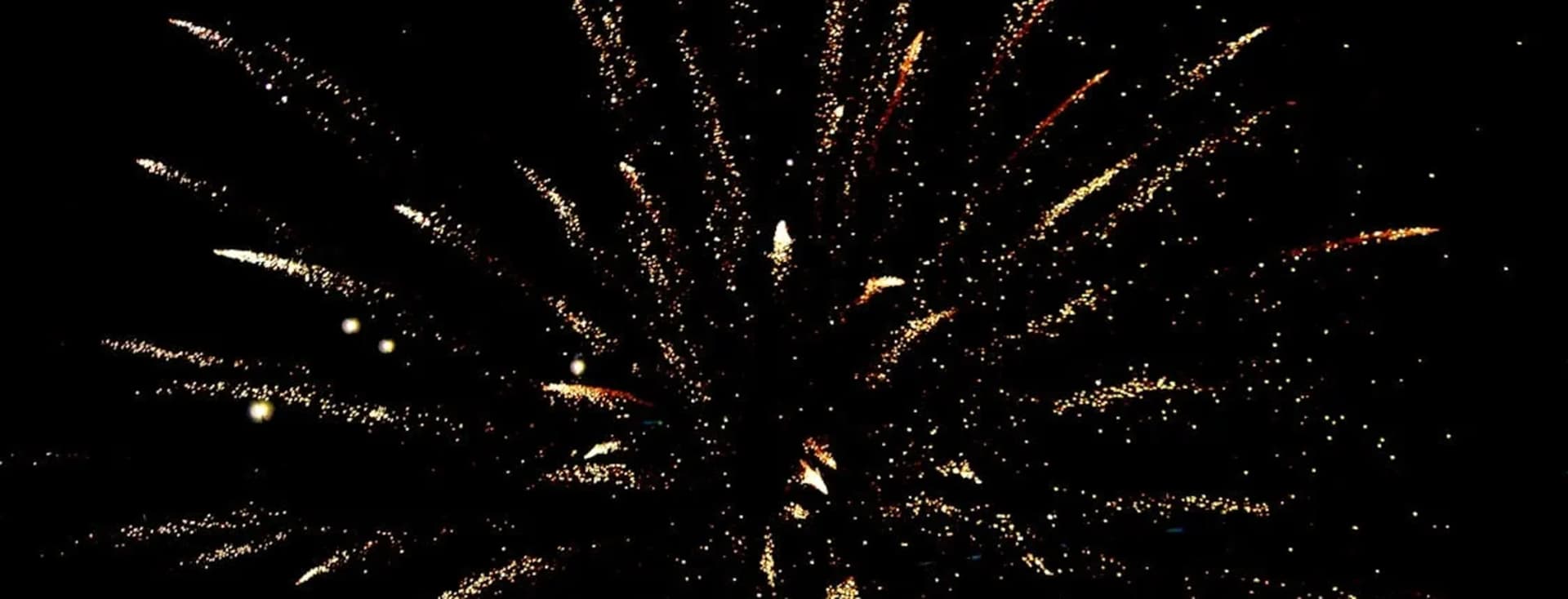 Des feux d'artifice dorés explosent sur un ciel nocturne noir, rayonnant vers l'extérieur en forme d'étoile.