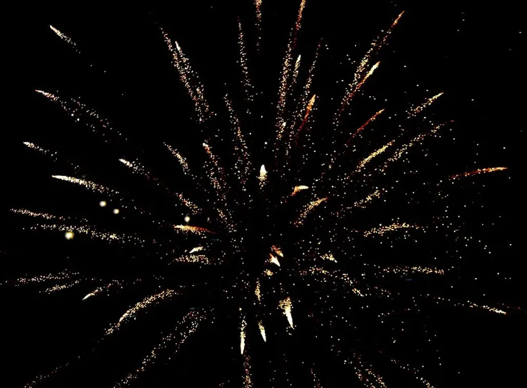 Gouden vuurwerk explodeert tegen een zwarte nachthemel en straalt in een stervorm naar buiten.