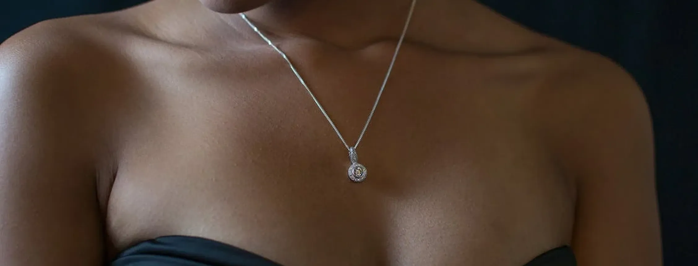Close-up of a woman wearing a black strapless top and a silver necklace with a round pendant.