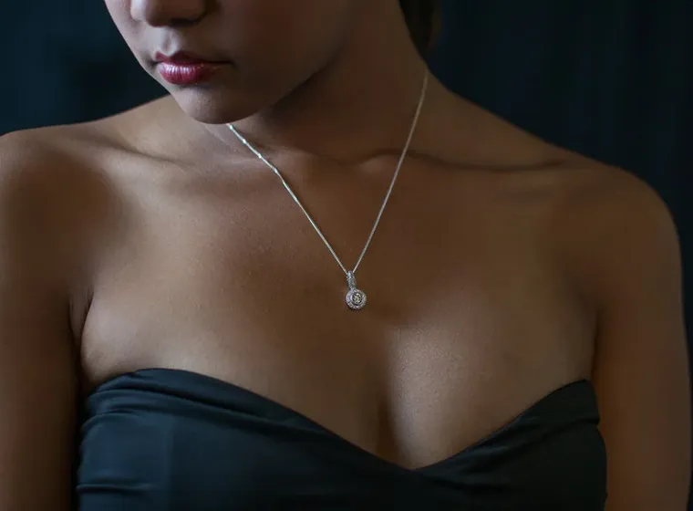Close-up van een vrouw die een zwarte strapless top draagt en een zilveren ketting met een ronde hanger.