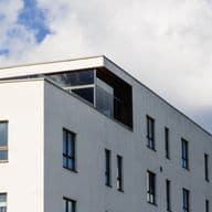 Modern white building with dark-framed windows against a blue sky with white clouds.