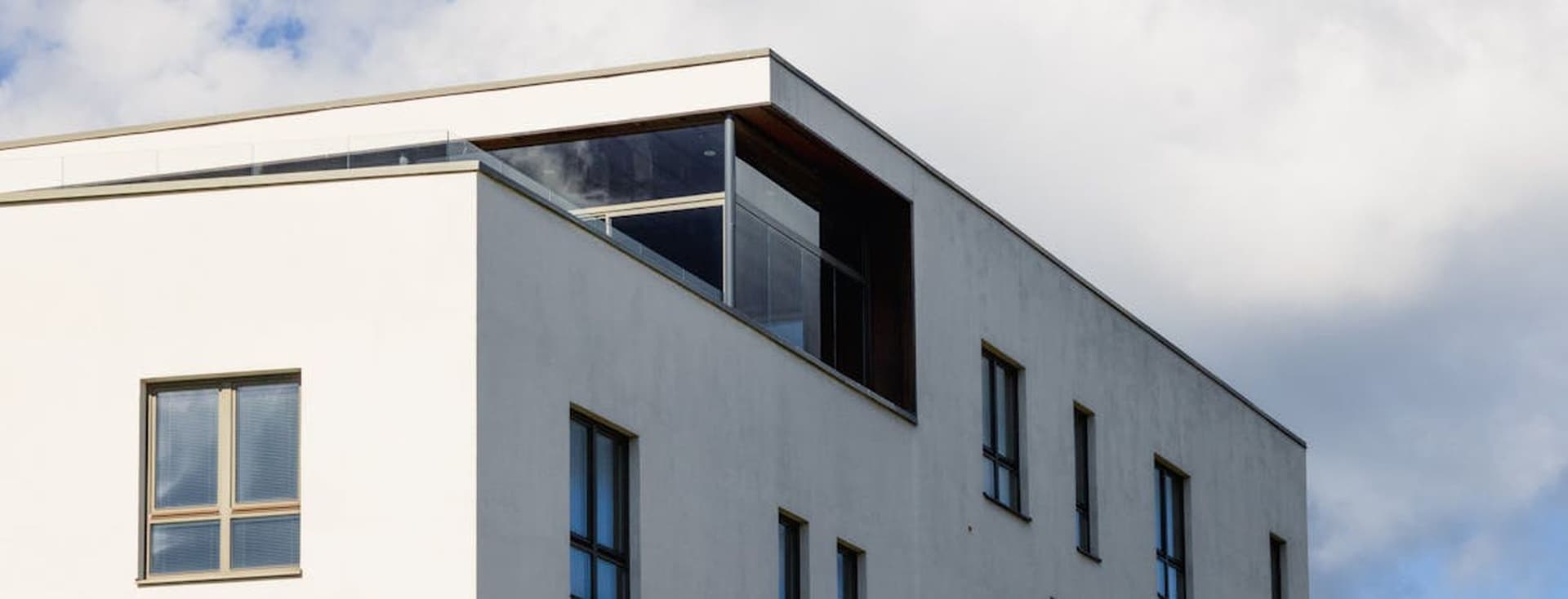 Bâtiment blanc moderne avec des fenêtres à cadre foncé sur fond de ciel bleu avec des nuages blancs.