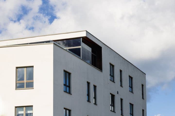 Bâtiment blanc moderne avec des fenêtres à cadre foncé sur fond de ciel bleu avec des nuages blancs.