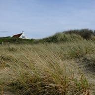 Beach house with red roof, seen from grassy dunes under a blue sky.